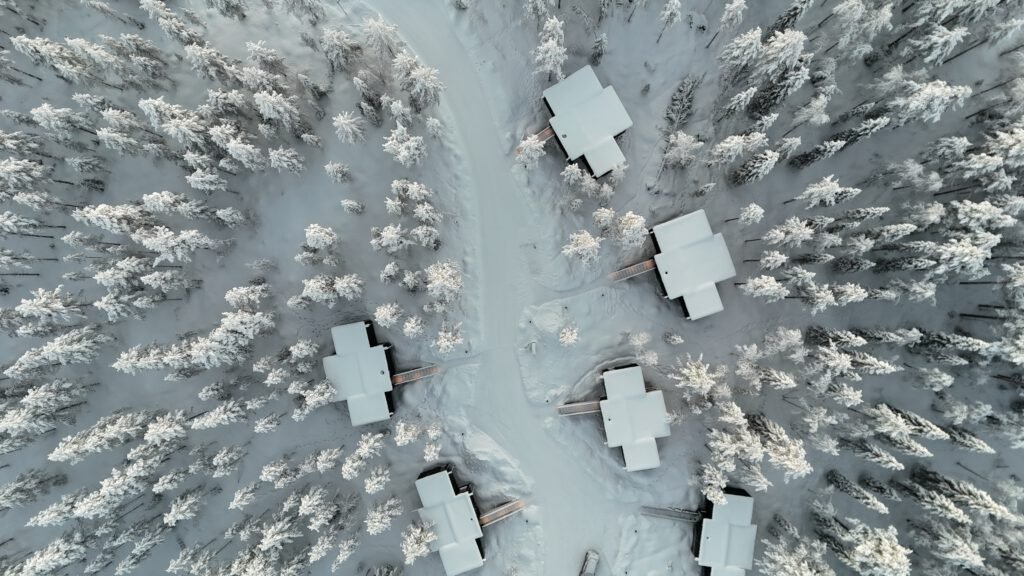 Top-down aerial view of NOA Villas cabins and snowy paths among forest trees.