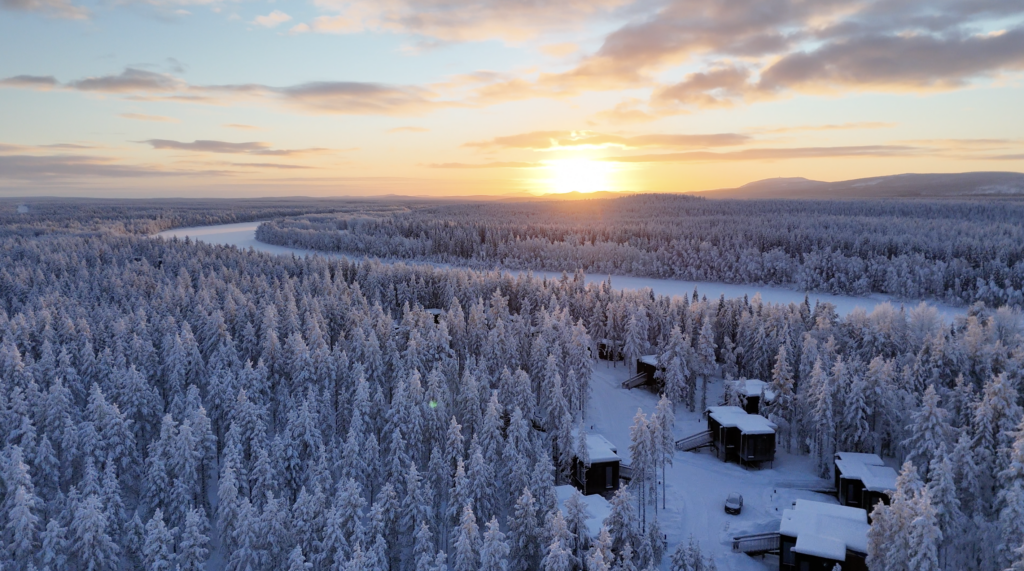 Aerial view of NOA Villas cabins among snow-covered Lapland forest at sunrise.
