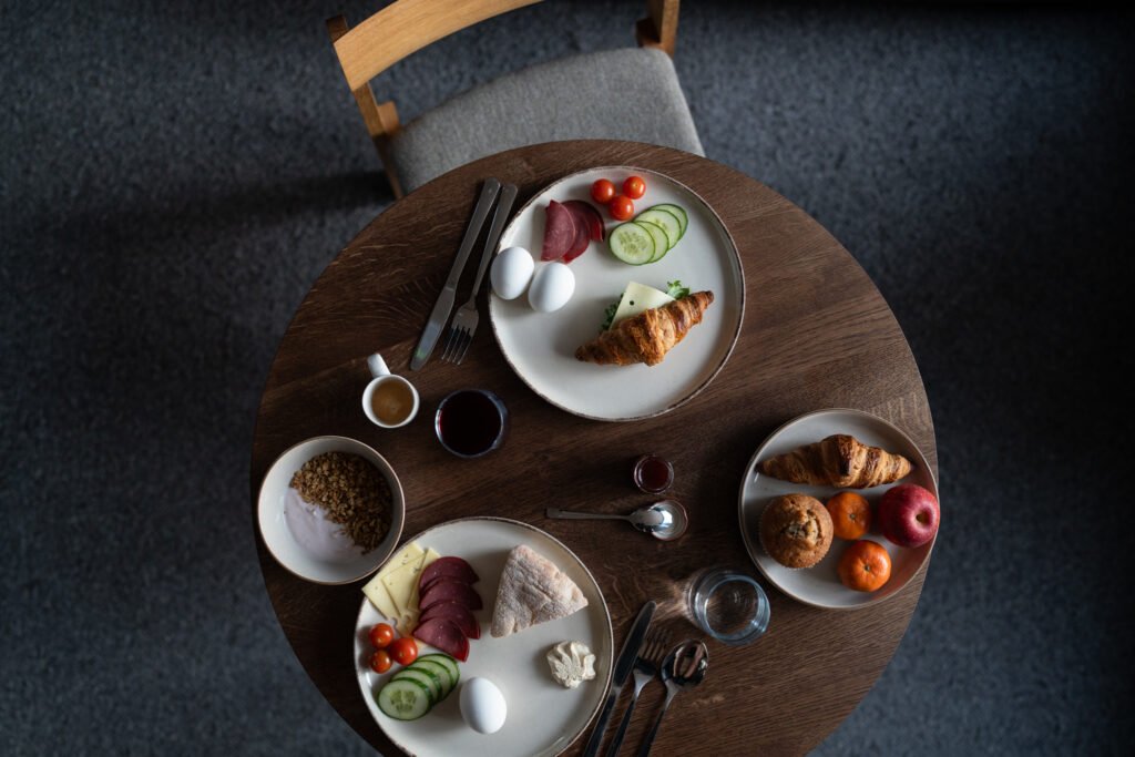 Breakfast spread with eggs, croissants, fruit, yoghurt and coffee arranged on a dining table.