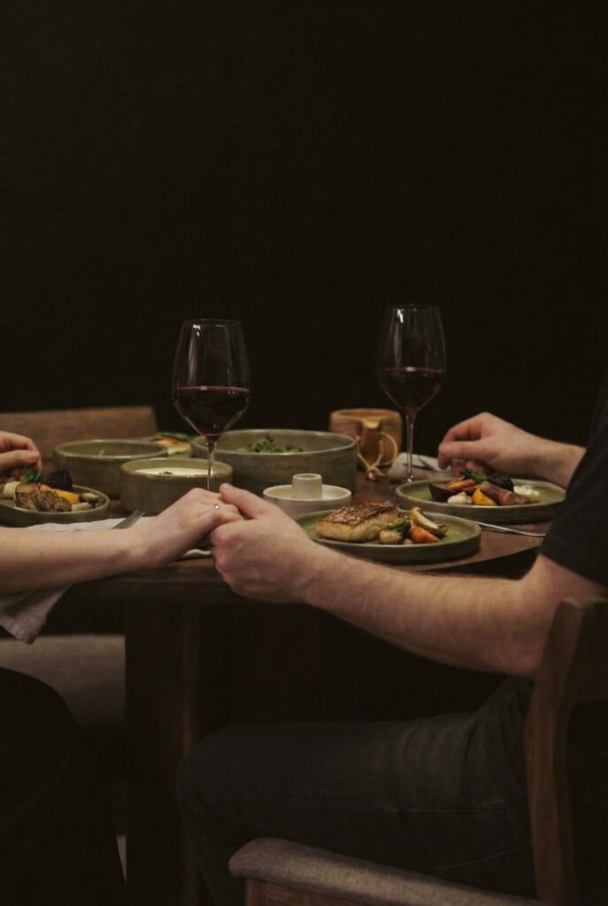 Guests sharing a candlelit meal with plated dishes and wine at a wooden table.