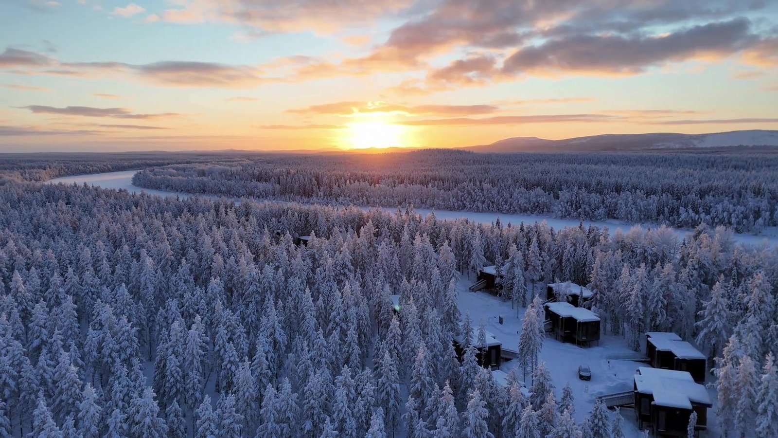 Aerial winter view of NOA Villas cabins among snow-covered forest at sunrise.