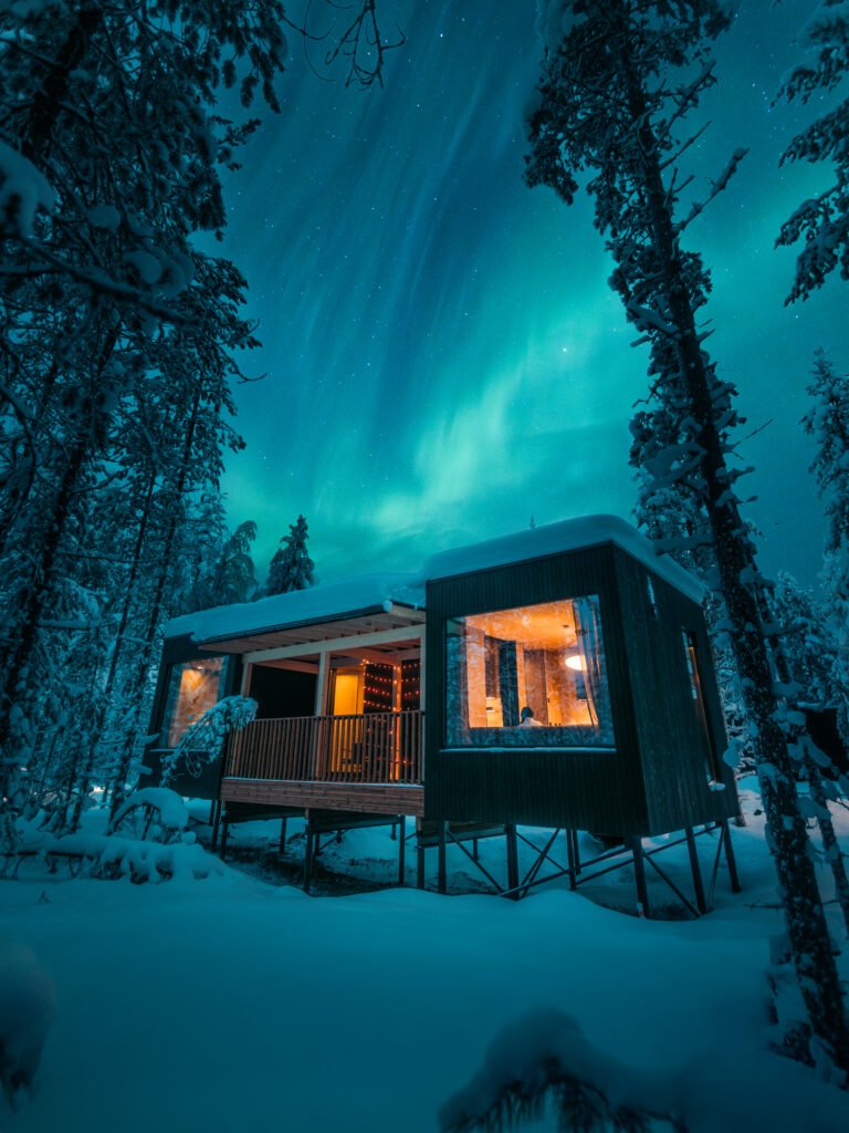 A dark villa glowing beneath the northern lights in a snowy Lapland forest.