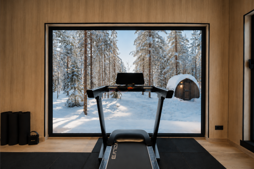 Treadmill in a private gym facing a large window with snowy Lapland forest outside.