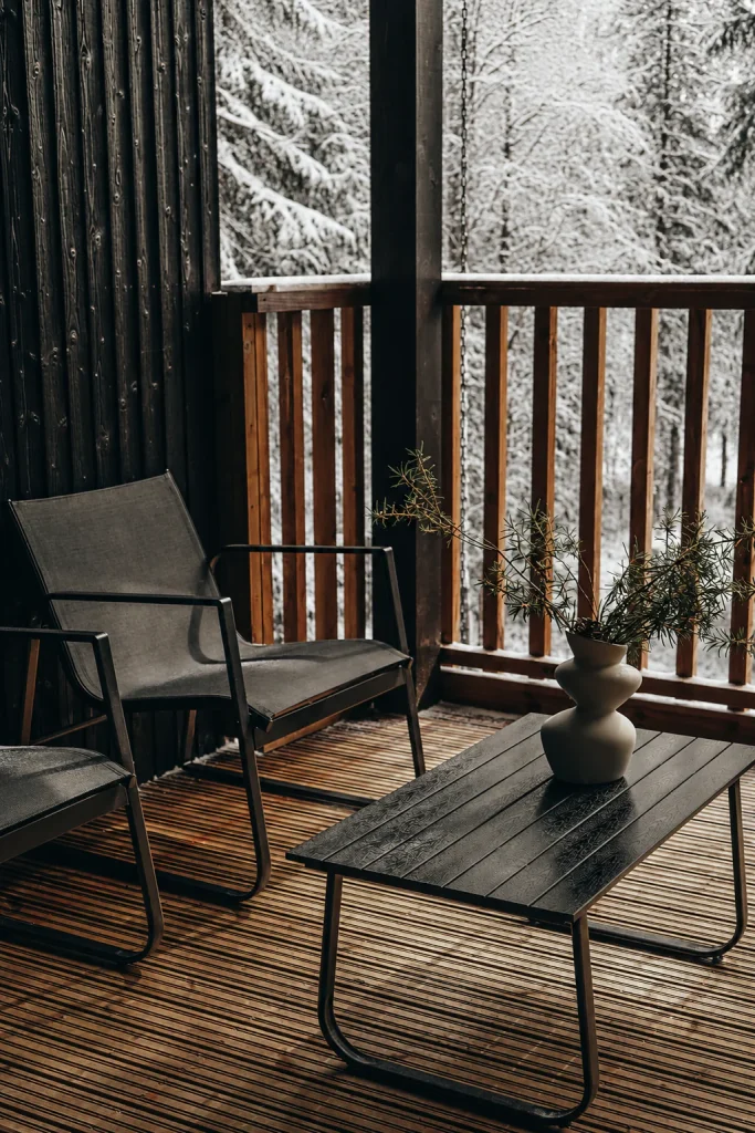 Covered Deluxe Villa terrace with lounge chairs overlooking a snowy pine forest.