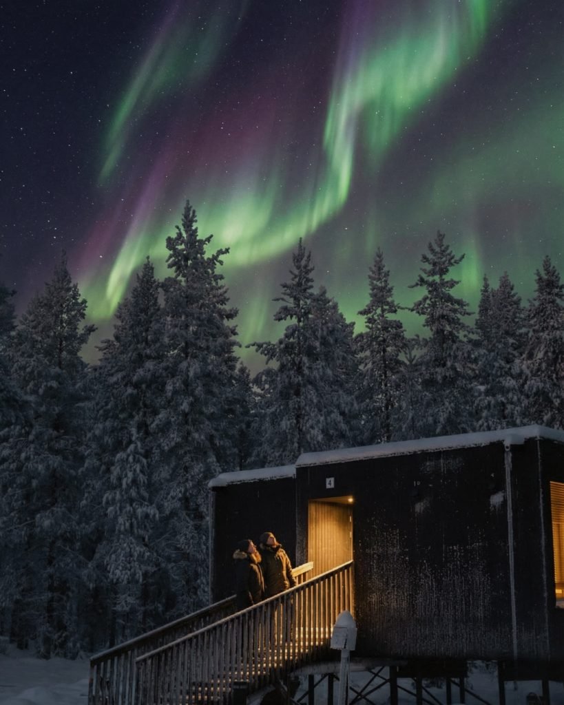 Northern lights above NOA Villas and a snow-covered Lapland forest.