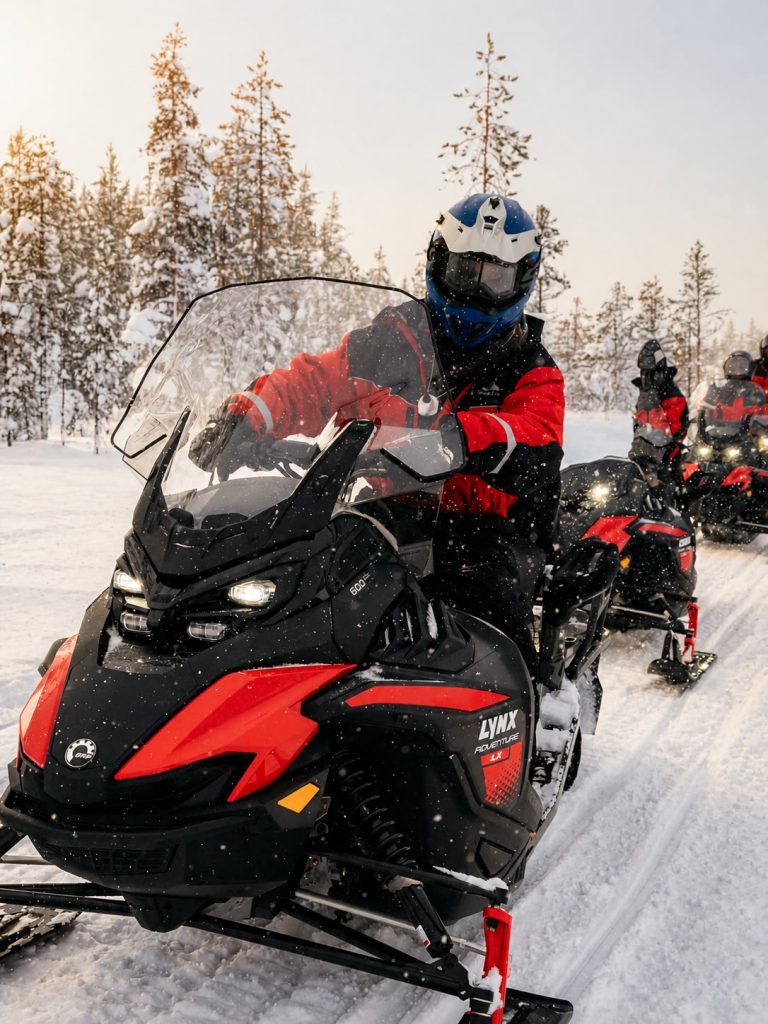 Guests riding snowmobiles through a snowy Lapland forest.