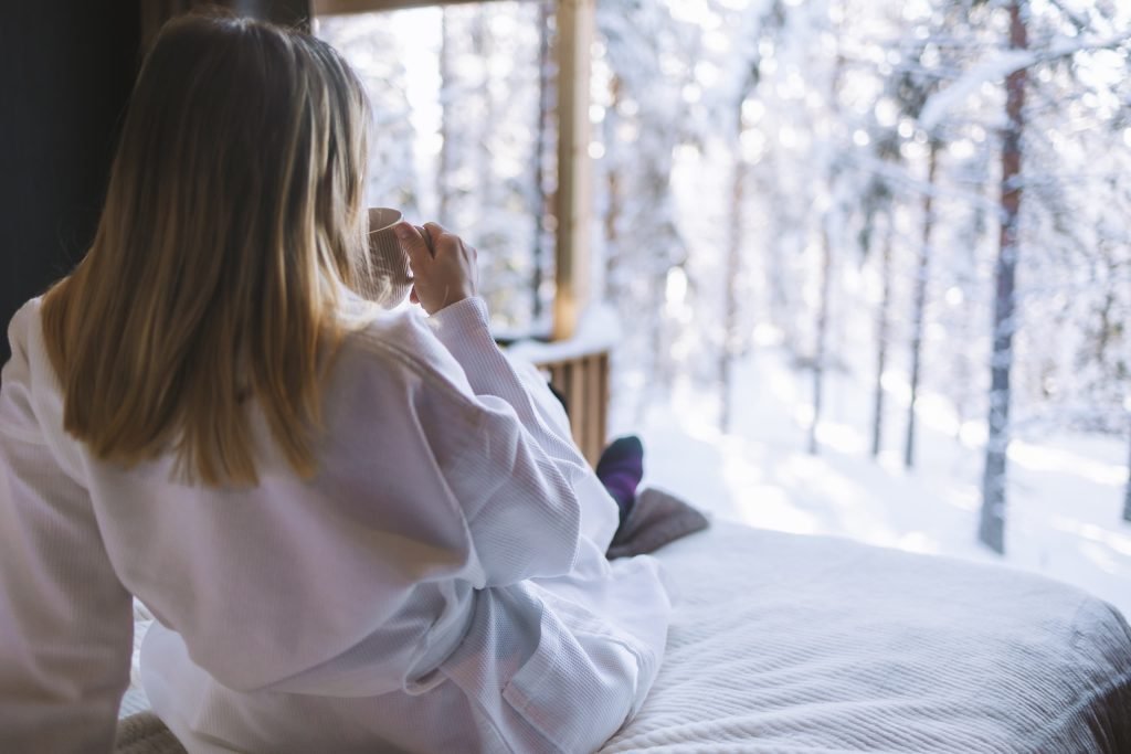 Guest relaxing in a villa bedroom overlooking a snowy Lapland forest.