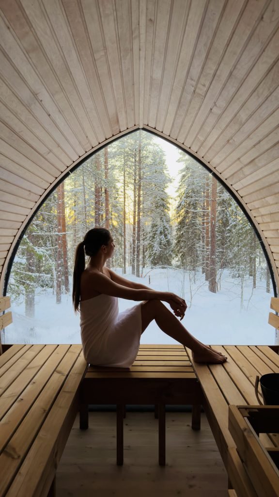 Guest relaxing in a panoramic sauna overlooking a snowy Lapland forest.