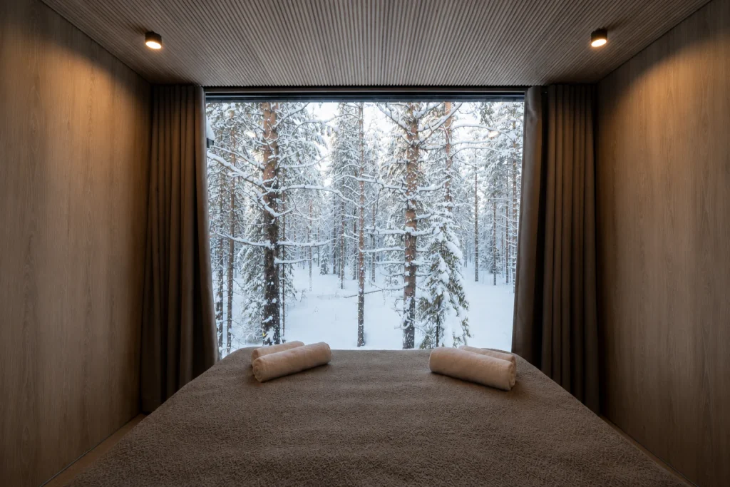 Standard Villa bedroom with a panoramic window overlooking the snowy pine forest.
